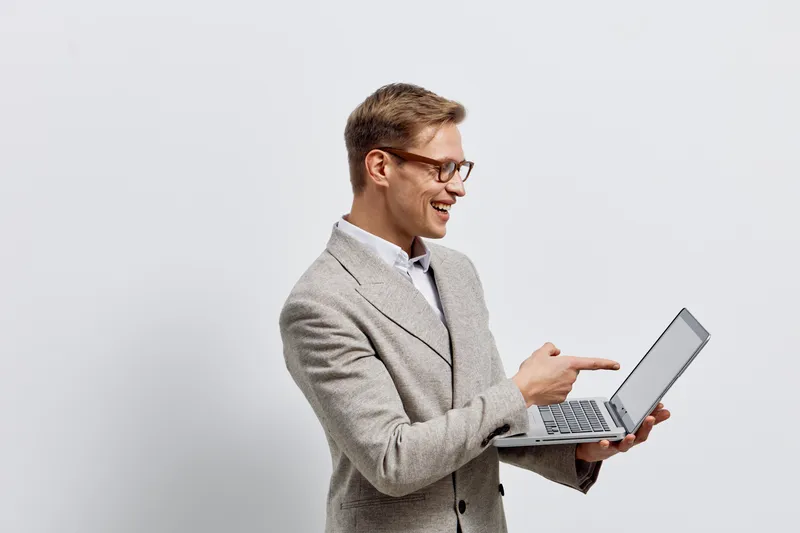 smiling man working on laptop holding pointing at screen wearing glasses beige jacket isolated on white background digital nomad concept