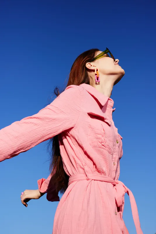 Stylish young woman in a pink dress enjoying the outdoors under a clear blue sky, exuding confidence and joy in her fashionable summer attire