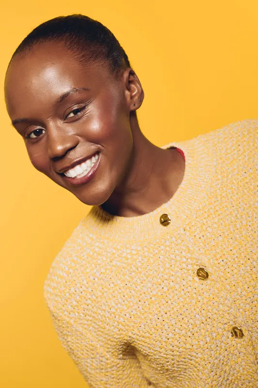 Close-up of smiling African woman with dark skin wearing yellow sweater against yellow background. Concept of happiness, beauty, fashion, and positive emotions in studio.