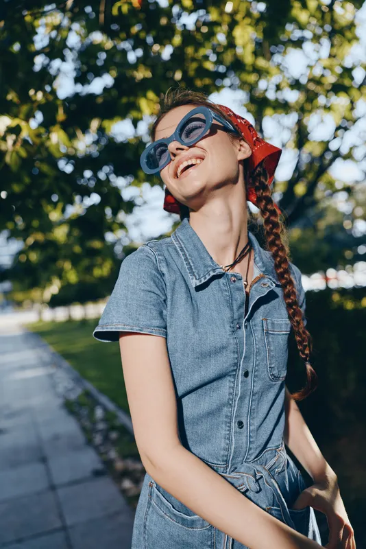 lifestyle woman in modern boho-western denim dress and red bandana smiling outdoors with natural green background, film color style, street style summer fashion