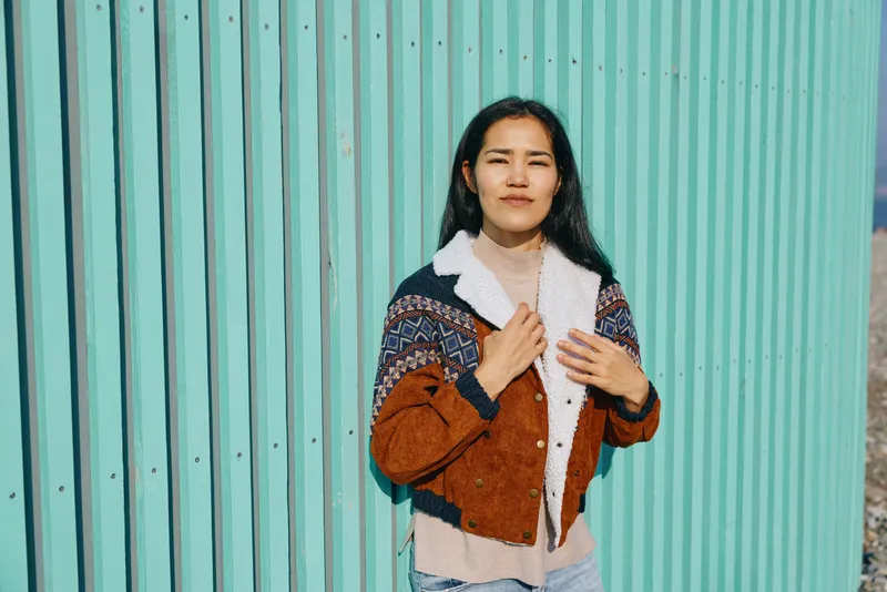 Fashion, style, jacket, outerwear worn by a confident female model against a vibrant teal wall outdoors in a casual streetwear pose, emphasizing texture, color, and contemporary look