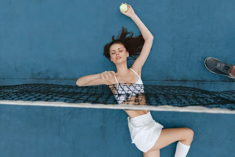 Active young woman practicing tennis skills on a blue court, showcasing athleticism and determination while holding a tennis ball in an energetic pose