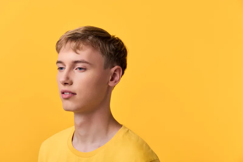 Youthful man wearing a yellow shirt against a bright yellow studio background, calm expression, clean lighting and minimalist composition for fashion, lifestyle or product mood stock image