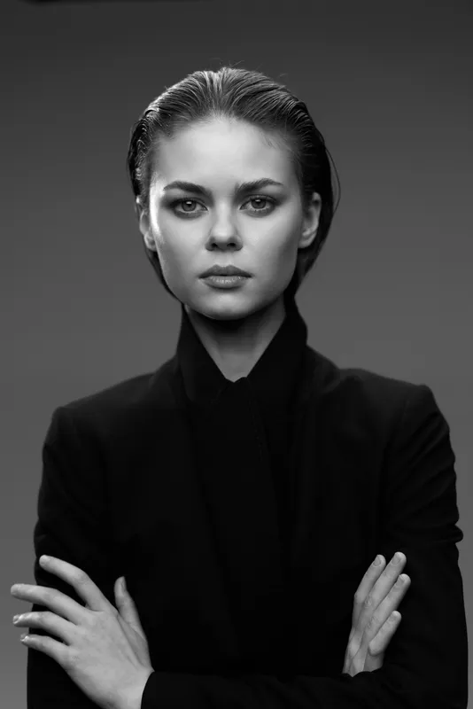 Black and white portrait of a confident woman in dark clothing with crossed arms and serious expression