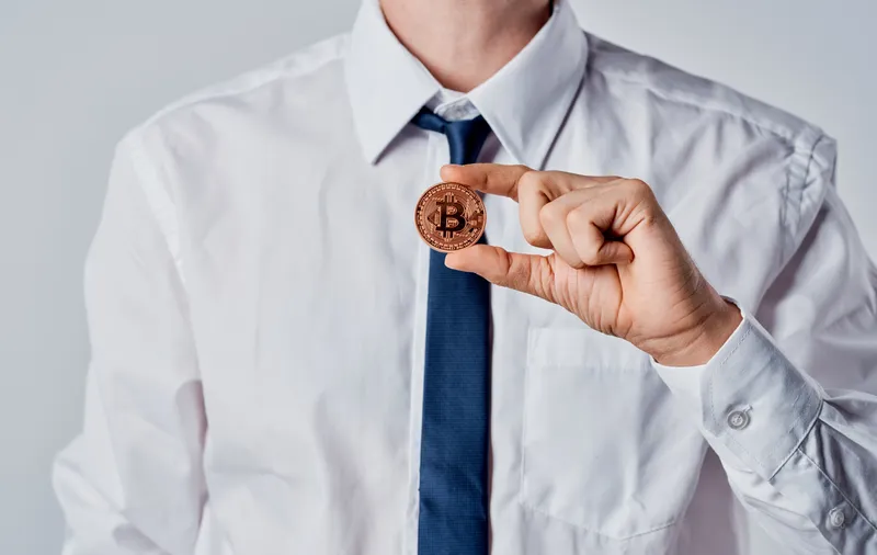 Бизнесмен в костюме на сером фоне, связанный с криптовалютой Bitcoin