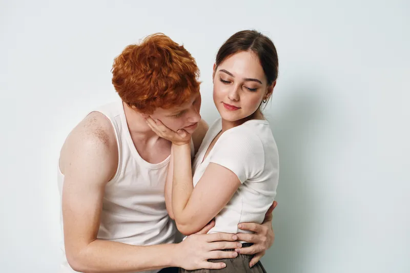 Couple, woman and man embracing with affection, love and tenderness in casual clothing on white background. Emotional connection, romance and intimate moment between two people.