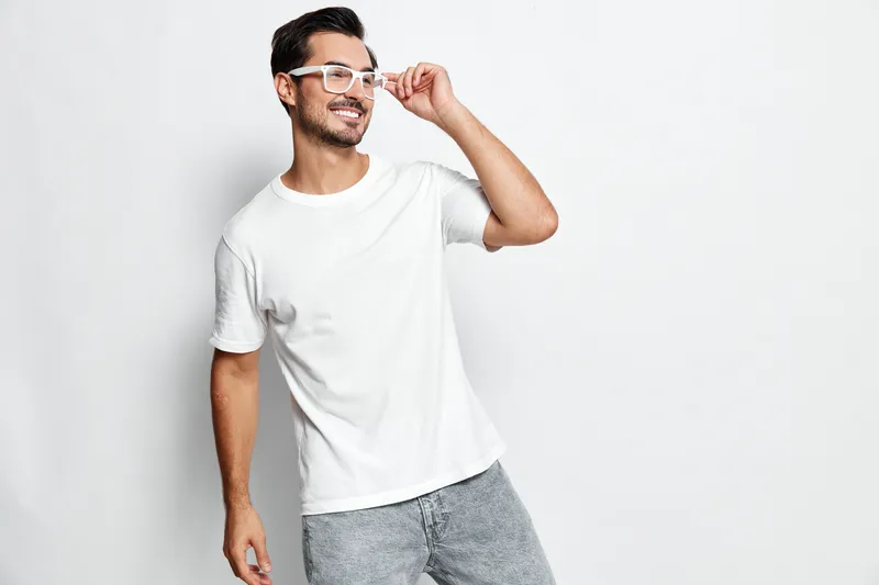 Full body smiling happy cheerful young man wearing casual white t-shirt and glasses, looking at camera, isolated on plain solid light background. People lifestyle concept