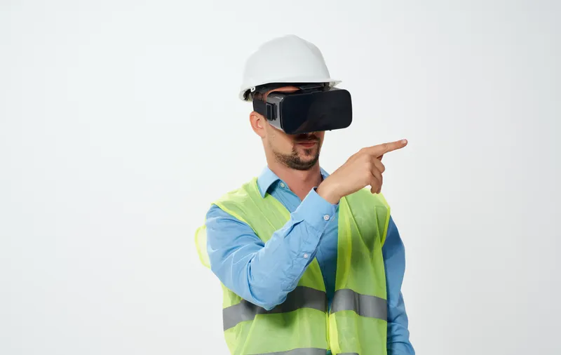 Архитектор в светоотражающем жилете и белой каске смотрит через 3D-очки виртуальной реальности