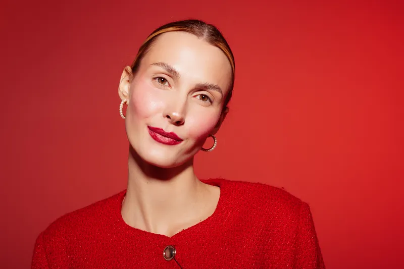 Portrait of confident woman with red lipstick and red sweater on red background. Studio lighting highlights natural skin texture and elegant facial expression. Beauty and fashion concept.