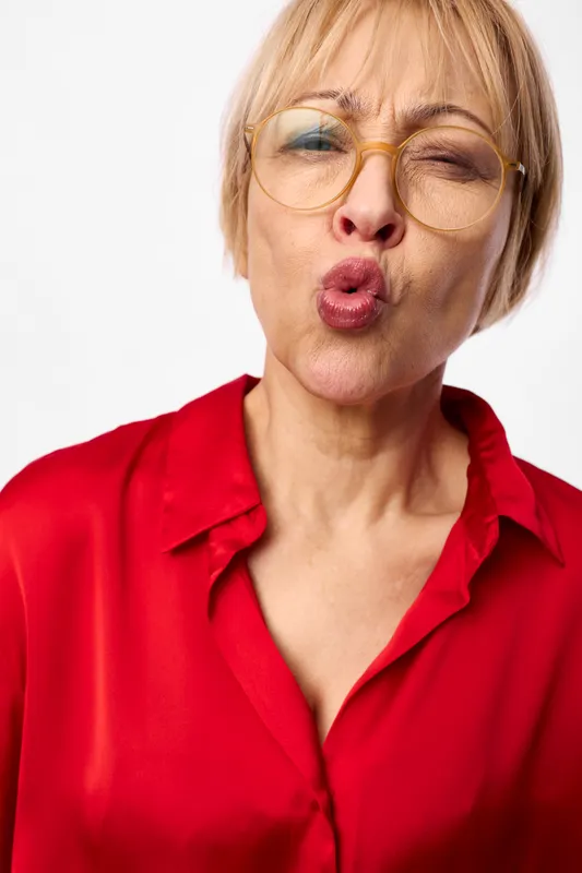 Woman portrait closeup making funny expression, tongue out and wink, red shirt on white background, playful mature age, studio headshot