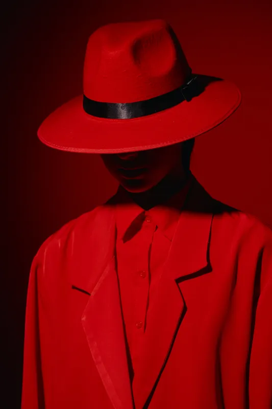 Fashion model wearing a bold red hat and matching coat in dramatic low light with deep shadows and minimal facial visibility. Concept of avantgarde beauty and creative styling.