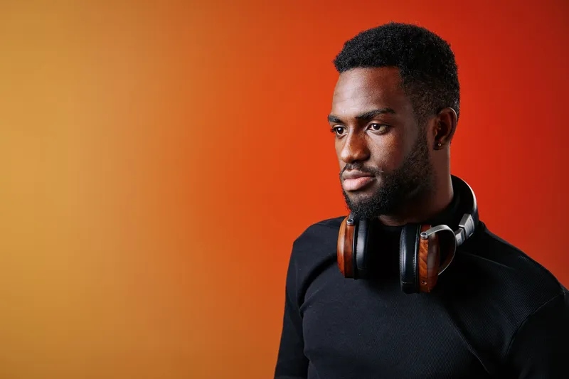 Portrait of a young African man with headphones looking thoughtfully against a warm gradient background, representing music and relaxation