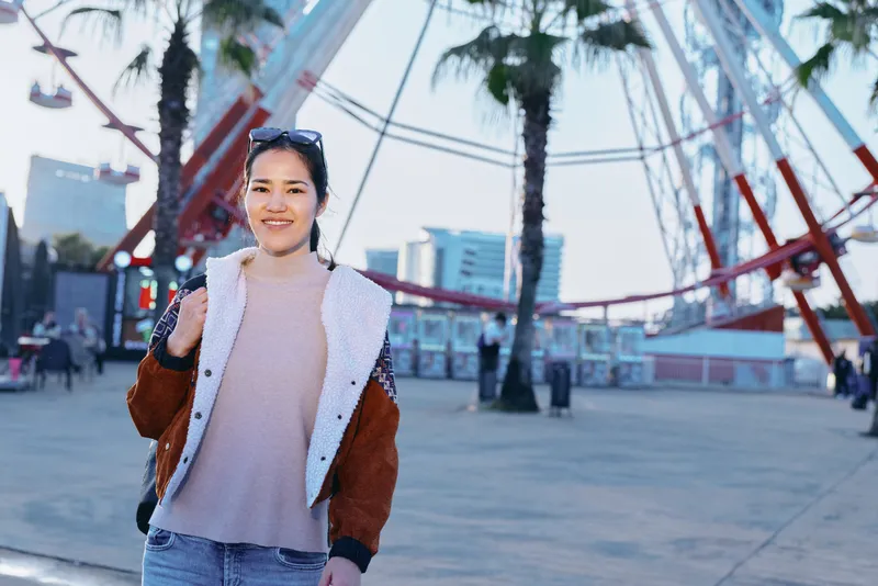 Woman, outdoor, smiling, fashion, street, urban, casual, plaza photography of a stylish traveler posing with confidence under palm trees in a bright urban setting, daylight highlighting modern style