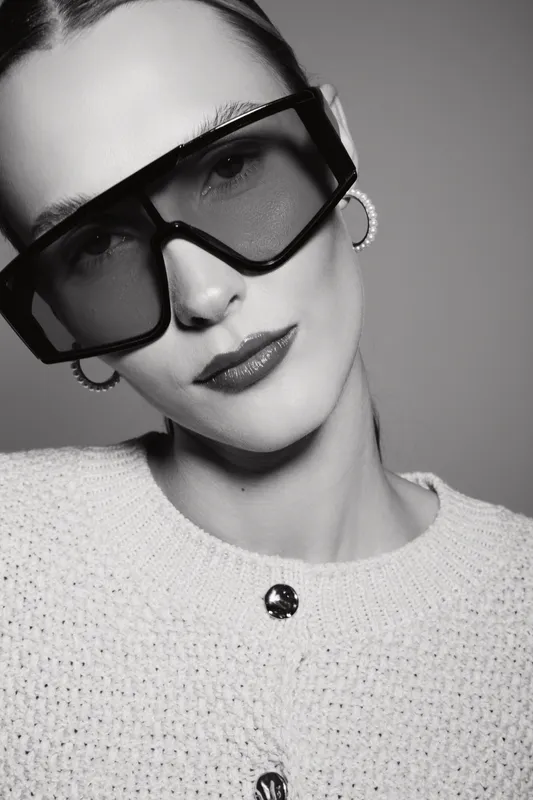Portrait of a fair skinned caucasian woman wearing oversized glasses and knitted sweater. Minimalistic black and white studio shot with elegant modern style and confident expression.
