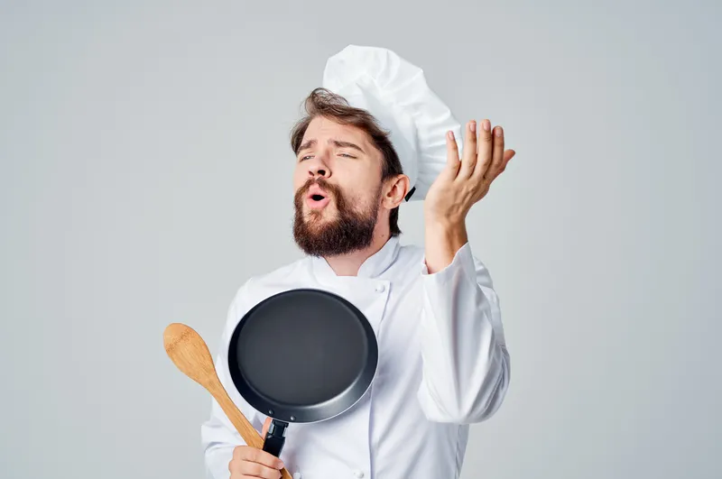 Шеф-повар держит сковороду и готовит еду на кухне ресторана