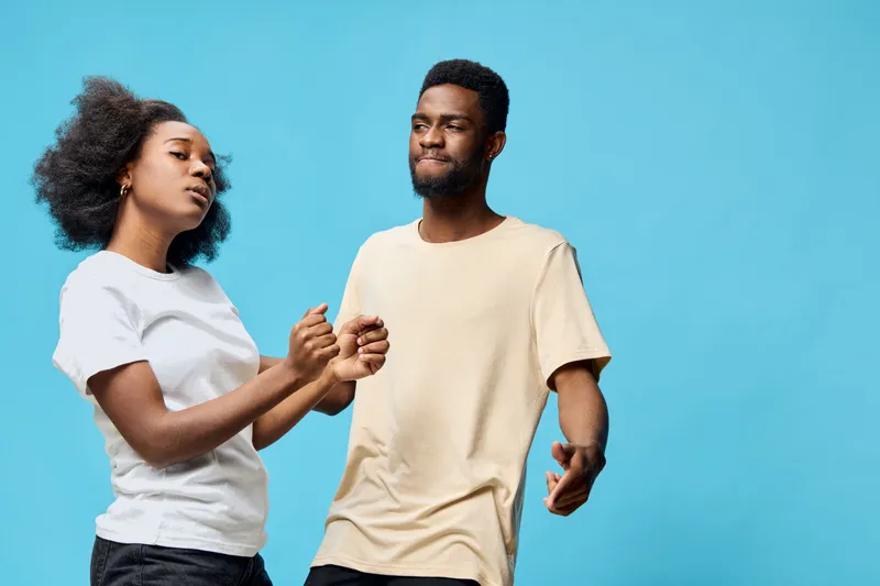 Young couple dancing joyfully against a light blue background, showcasing carefree emotions and stylish casual attire, perfect for celebration concepts