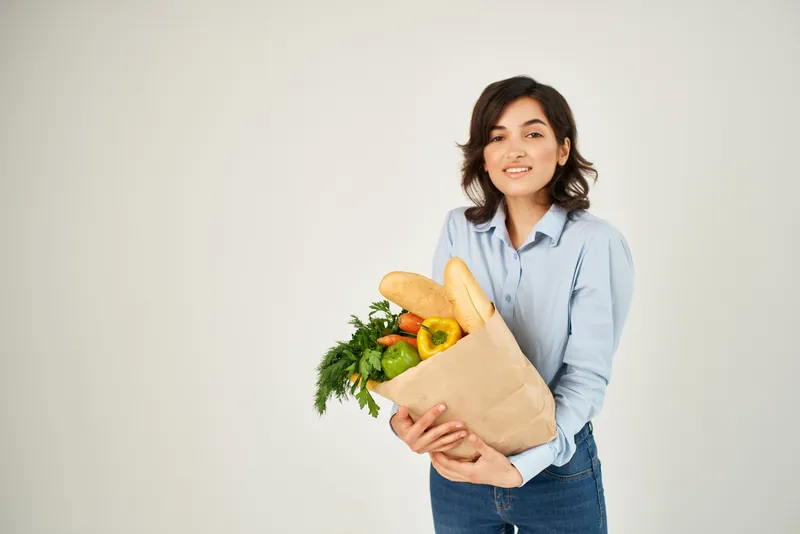 Брюнетка в голубой рубашке с пакетом продуктов из супермаркета