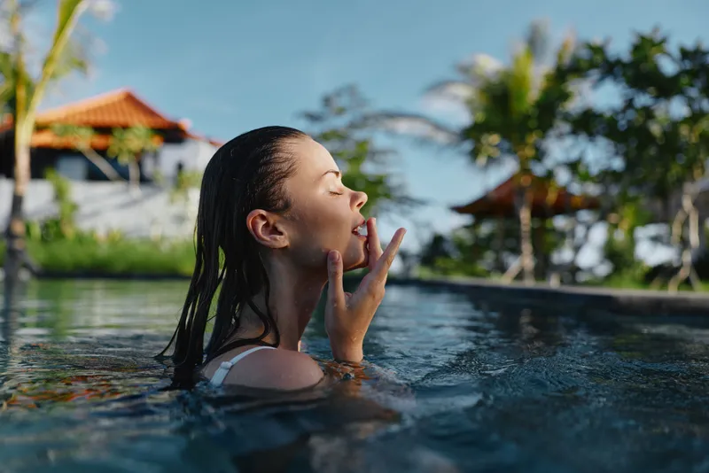 A woman relaxes in a bright pool, eyes closed as she breathes in the sun and breeze. Outdoor leisure and summer mood highlight carefree wellness and self care by the water.