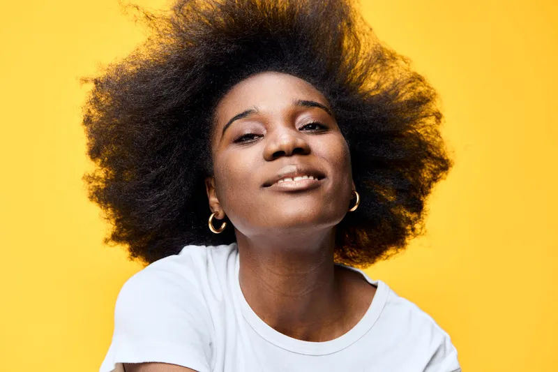 Confident African woman smiling with natural textured hair on a bright yellow background, showcasing beauty and self acceptance in a vibrant portrait