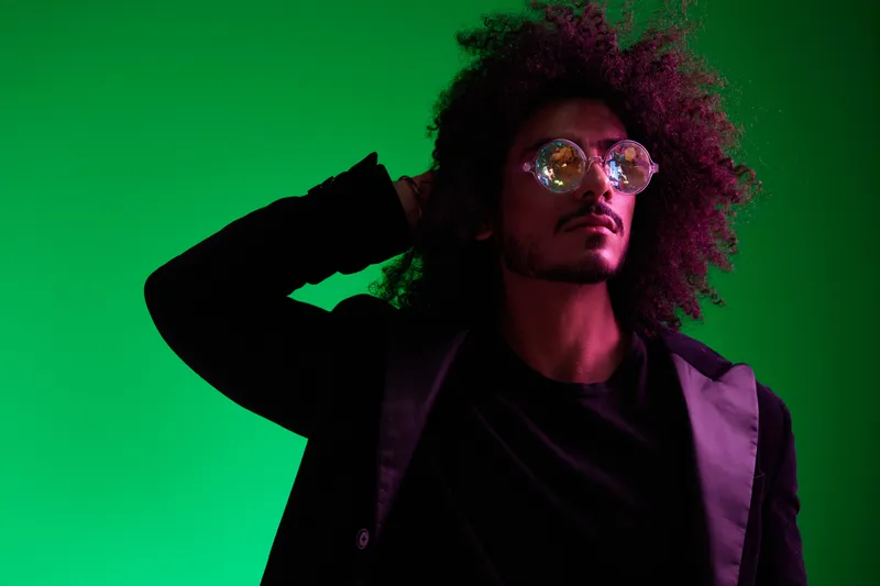 Модный портрет мужчины с кудрявыми волосами на зелёном фоне, в солнцезащитных очках, мультинациональный образ, розовый цветовой акцент, стильно, современно