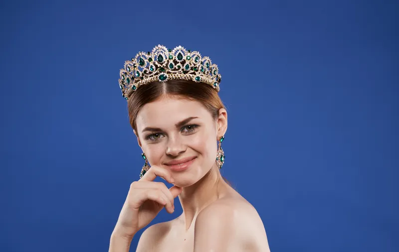 Красивая женщина с диадемой на голове на голубом фоне, королева красоты с серьгами, макияж, модель