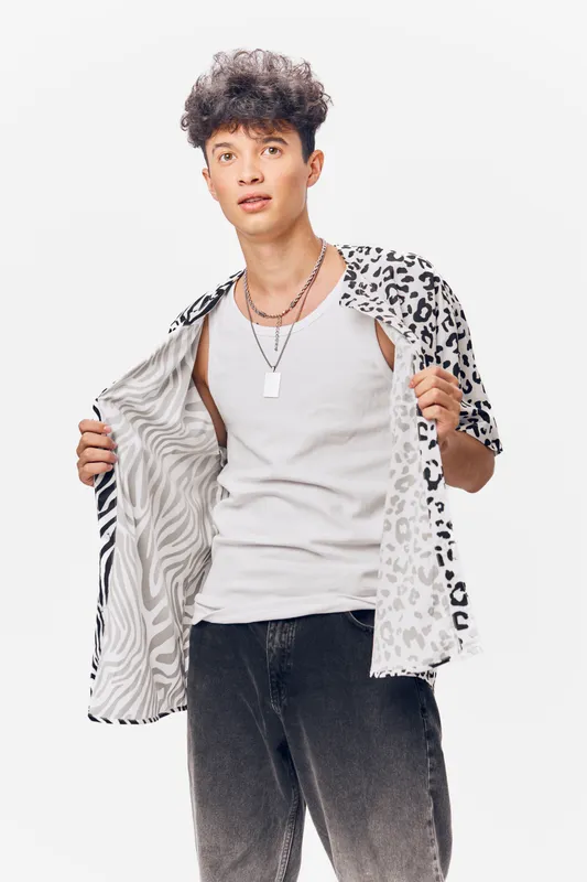 young man wearing patterned shirt open over white tank top, stylish casual outfit with layered necklaces, isolated on white background, trendy fashion look