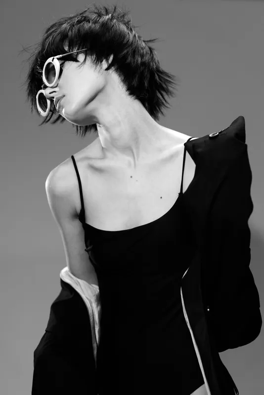 Black and white portrait of a stylish woman with sunglasses and short hair in a fashion pose and elegant outfit.