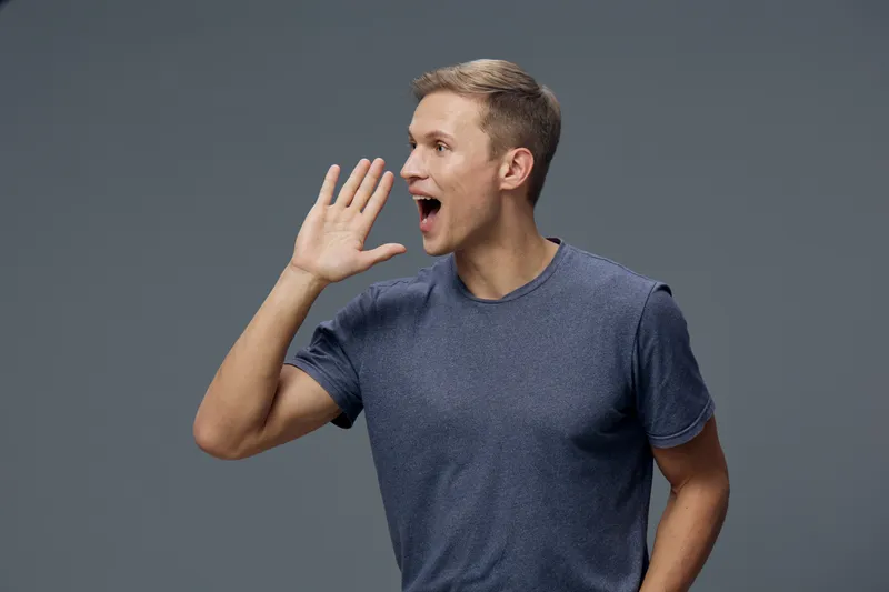 Smiling man with short hair wearing casual blue t-shirt, showing surprised expression, looking to the side, on plain gray background, studio portrait, people emotion concept, positive mood, casual sty