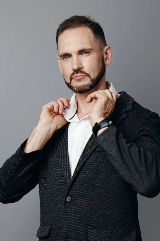 A business professional man adjusts his blazer, exuding confidence and focus against an isolated colored background. He communicates readiness for leadership, presenting a formal, composed demeanor