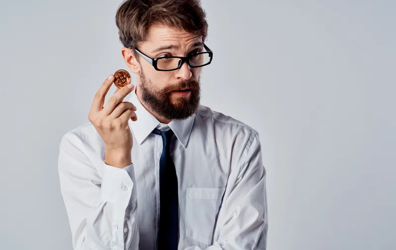 Бизнесмен в костюме на сером фоне с криптовалютой Bitcoin