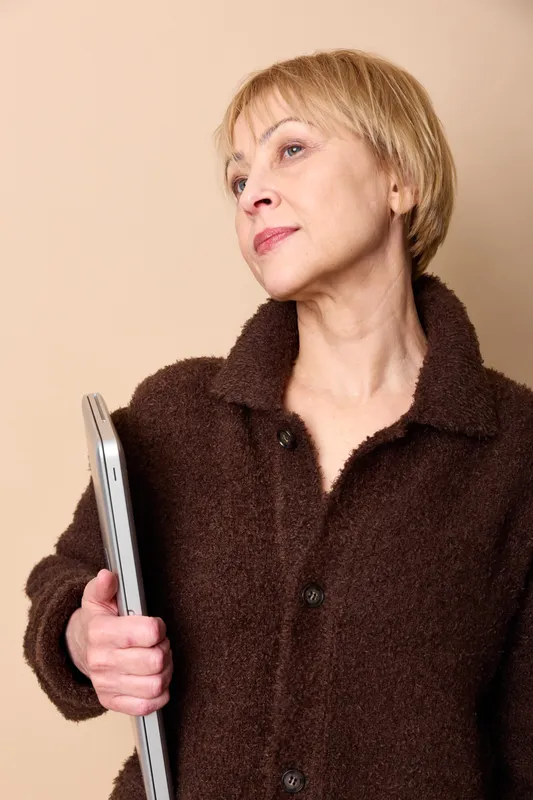 Thoughtful senior woman in studio portrait holds a tablet, looking away with expression. Technology and digital communication concept for lifelong learning and independence today.