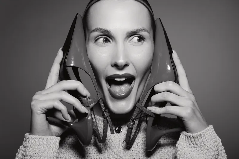 Happy Caucasian woman with light skin holds red high heels near her face, expressing joy and excitement. Concept of fashion, shoes, and female lifestyle with studio lighting.