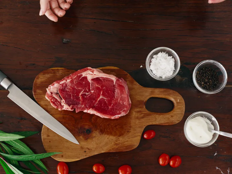 Женщина с ножом в руке нарезает свежее мясо стейка для жарки на кухне