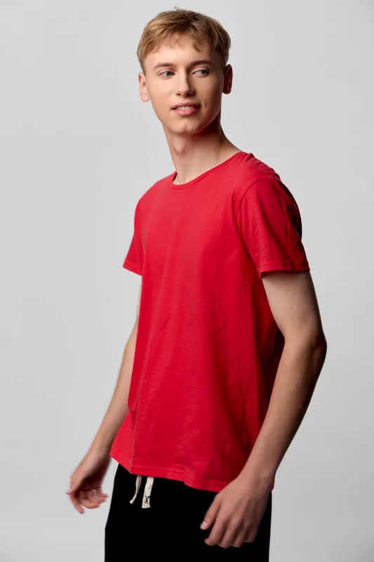 Young man in a red t shirt stands against a neutral backdrop, showcasing casual wear and relaxed style, ready for fashion catalog use, lifestyle shoot, or product collaboration in studio conditions