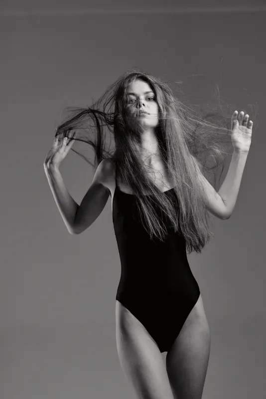 Black and white portrait of a young woman in a black leotard with flowing hair and expressive pose.