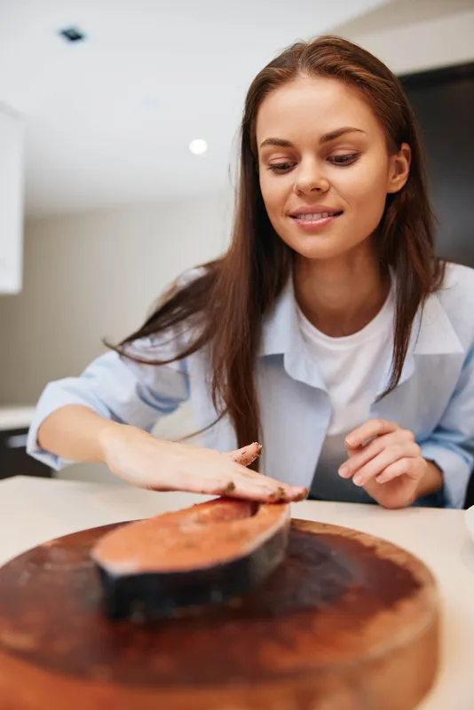 Молодая женщина нарезает мясо на разделочной доске на кухне, готовя ужин