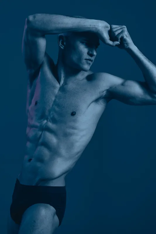 Dynamic man posing in a blue-toned, black and white image, showcasing strength and athleticism with confidence and artistry. Captivating and striking visual aesthetic.