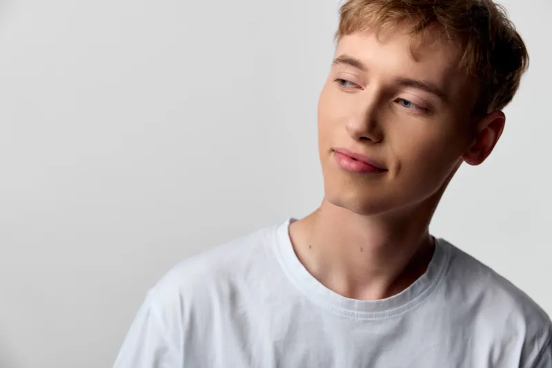 Young man casual clothing white t shirt thoughtful expression looking away, studio lighting calm mood relaxed vibe clean background simple setup fashion lifestyle image