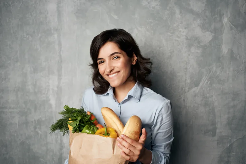 Улыбающаяся брюнетка с продуктовым пакетом в супермаркете, овощи, диетическое питание