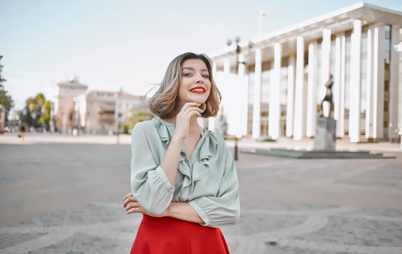 Женщина в рубашке и юбке прогуливается по центральным улицам города, на заднем плане видны высотные здания