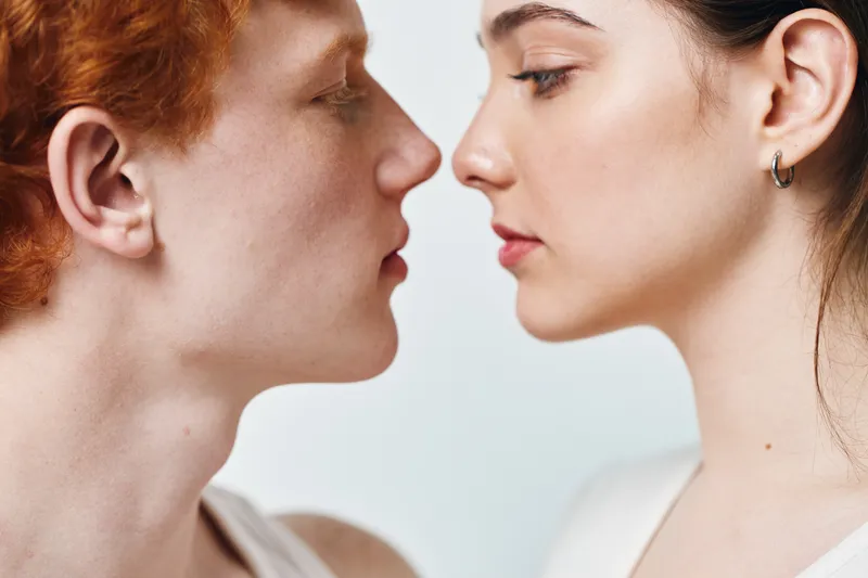 Couple close together with intimacy and focus on faces, young man and woman with natural expression looking at each other in tender moment with white background.