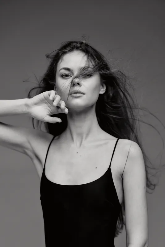 Black and white portrait of a young woman with flowing hair in a minimalist black dress, expressing calm and confidence.