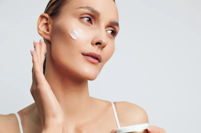 Woman skincare beauty face moisturizer cream on cheek, natural young woman portrait, calm spa treatment mood, isolated minimal studio background, hydration and facial care