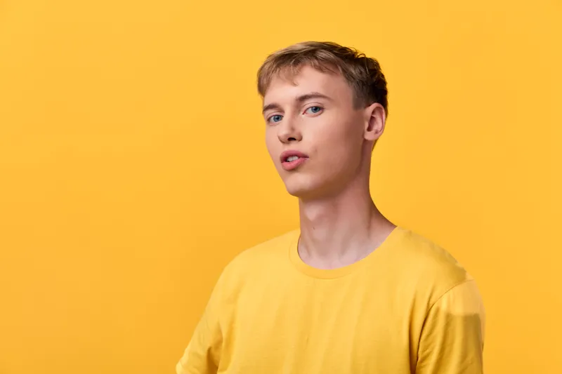 Male model wearing a yellow tee against a bright yellow backdrop, casual pose, clean studio setup, soft lighting, confident relaxed expression, vibrant monochrome color scheme and minimal styling