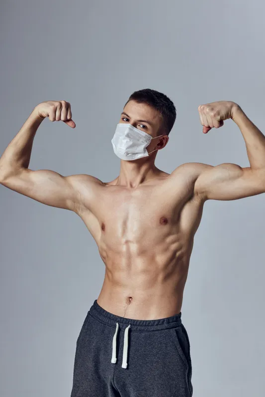 Спортивный мужчина с накачанным телом позирует в медицинской маске на изолированном фоне