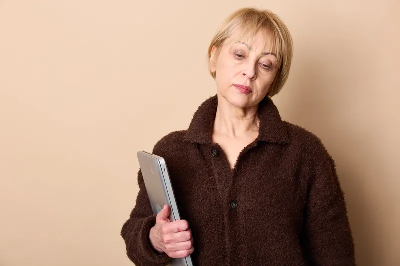Elderly woman holding a smartphone in a studio portrait, beige background, focused expression, communication and technology concept for daily life, soft light