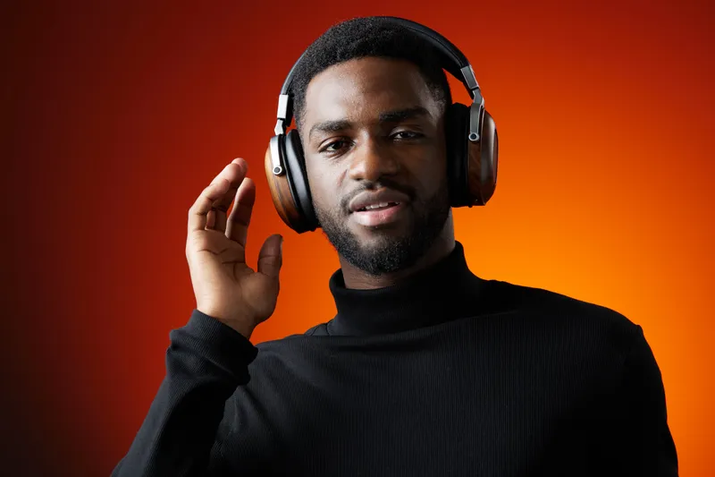 Young Black man wearing headphones, enjoying music with a confident expression against a warm orange background Perfect for lifestyle and music related concepts