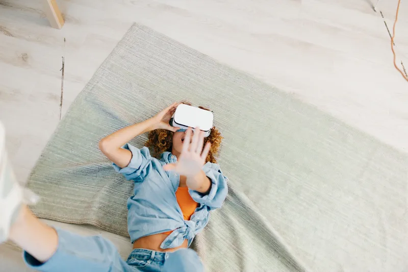 Улыбающаяся женщина наслаждается игрой в виртуальной реальности в VR-очках дома: футуристическая indoor-технология