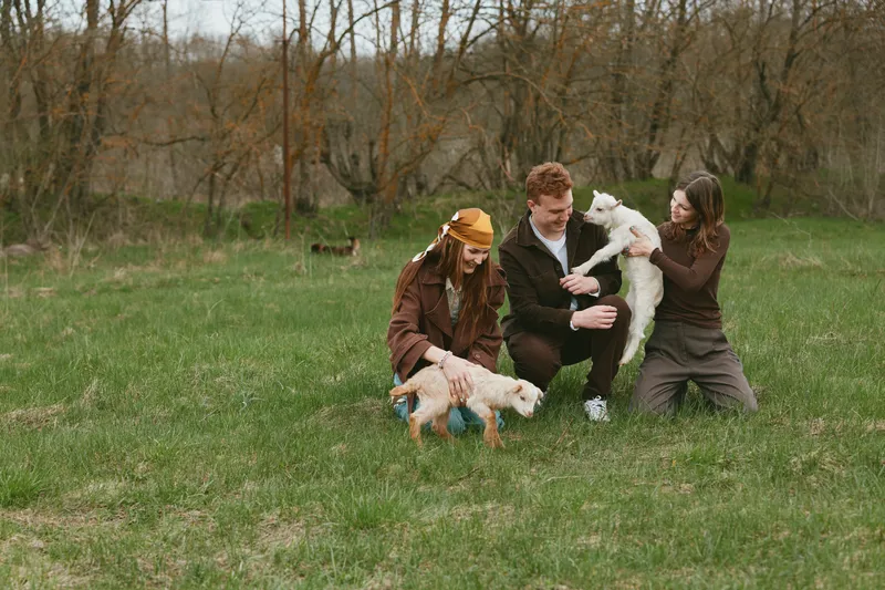 Joyful family outdoors in a park shares smiles while playing with dogs and a young goat kid, capturing playful interaction, nature, and relaxed lifestyle. Natural light highlights warm mood, casual