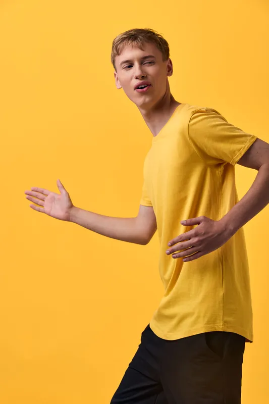 Dynamic man in a yellow shirt demonstrates movement in a bright studio, showcasing energy and fashion, ideal for lifestyle and dance themed projects and campaigns